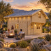 Opposite-side view of the Northwood Grand SD 70mm Freedom Loft Studio at golden hour. Four adults socialize around a fire feature while the warmly illuminated backyard bar is visible through the windows.
