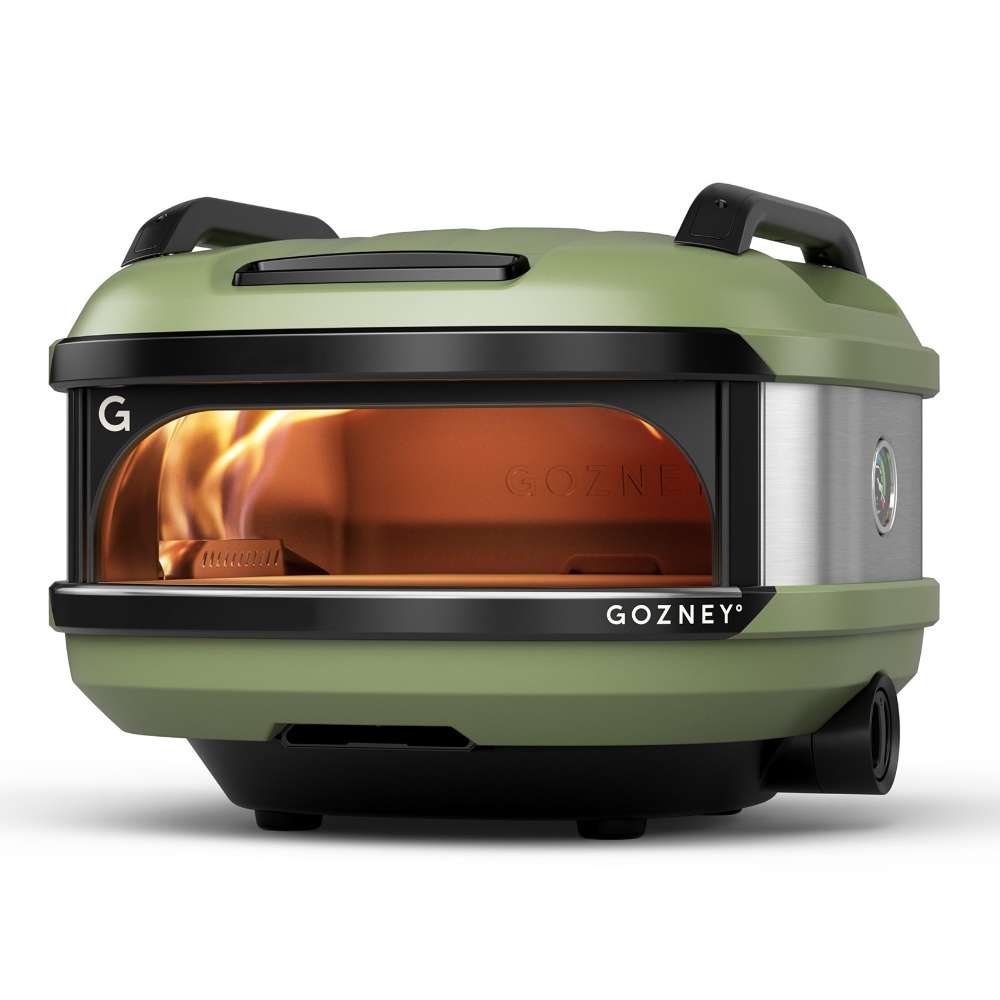 Olive Gozney Tread Pizza Oven angled front view on white with a flame inside the copper-toned dome the green shell and a rear wheel visible.