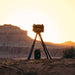 Olive Gozney Tread Pizza Oven silhouetted on its tripod stand at sunset in a desert landscape with red rock cliffs behind and a gas cylinder on the ground.