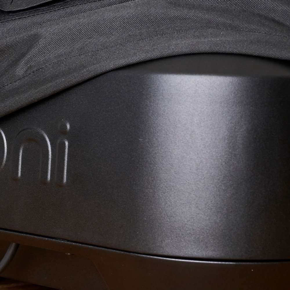 Ooni Volt Pizza Oven Cover close-up of the black woven hem draped over the matte dark gray oven body with the embossed ooni wordmark below it.