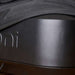 Ooni Volt Pizza Oven Cover close-up of the black woven hem draped over the matte dark gray oven body with the embossed ooni wordmark below it.