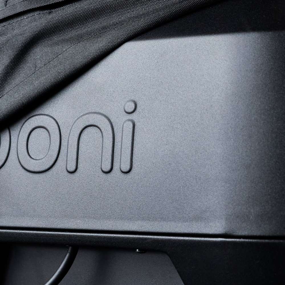 Ooni Volt Pizza Oven Cover close-up of the fabric edge lifted off the oven front, showing the embossed ooni wordmark and the base of the oven below.