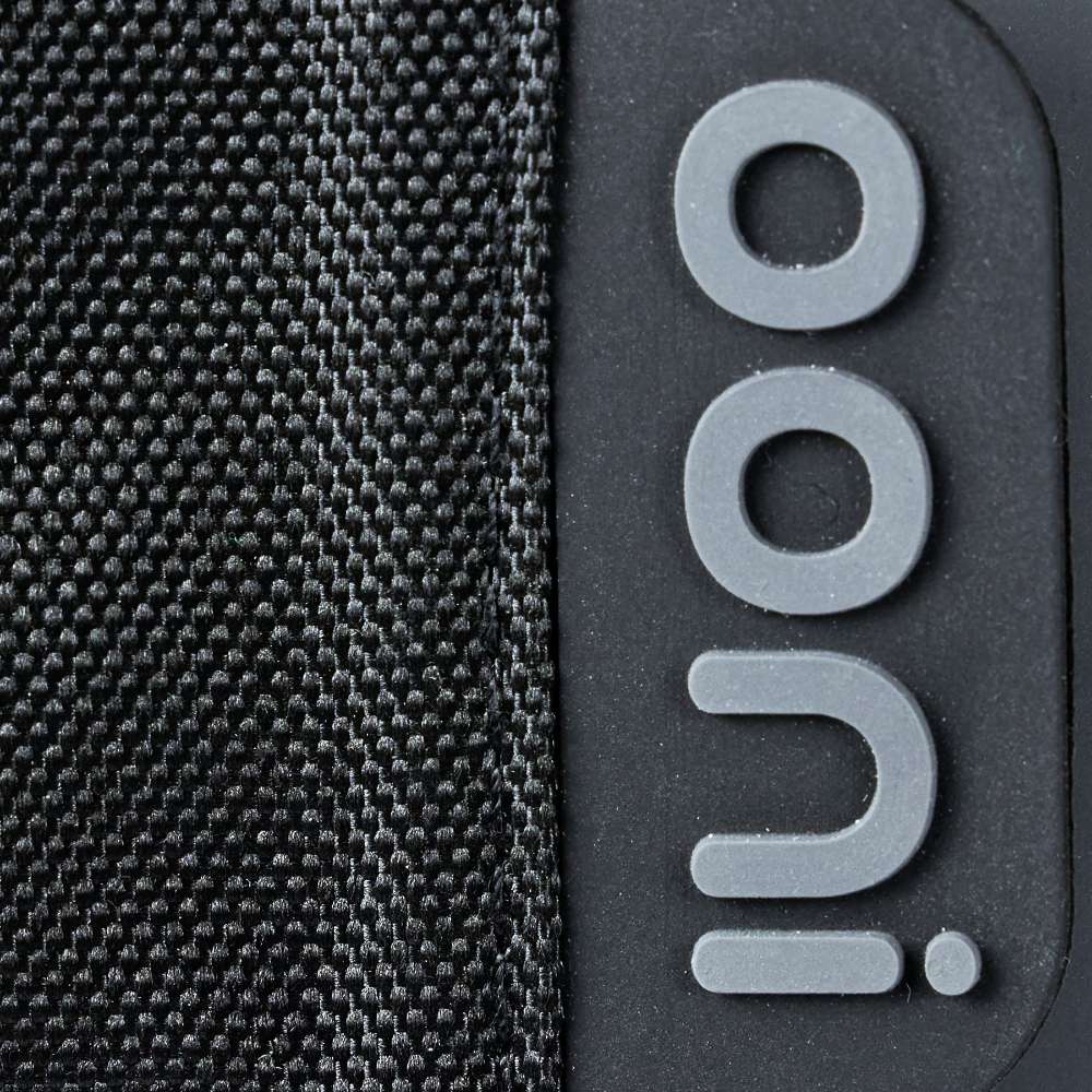 Ooni Volt Pizza Oven Cover close-up of the stitched black woven edge beside the raised gray ooni badge on the smooth dark panel.