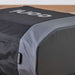 Ooni Volt Pizza Oven Cover laid over the oven on a wooden countertop indoors, seen from above with the white ooni logo on the black top panel and a small gray ooni tag at the side.