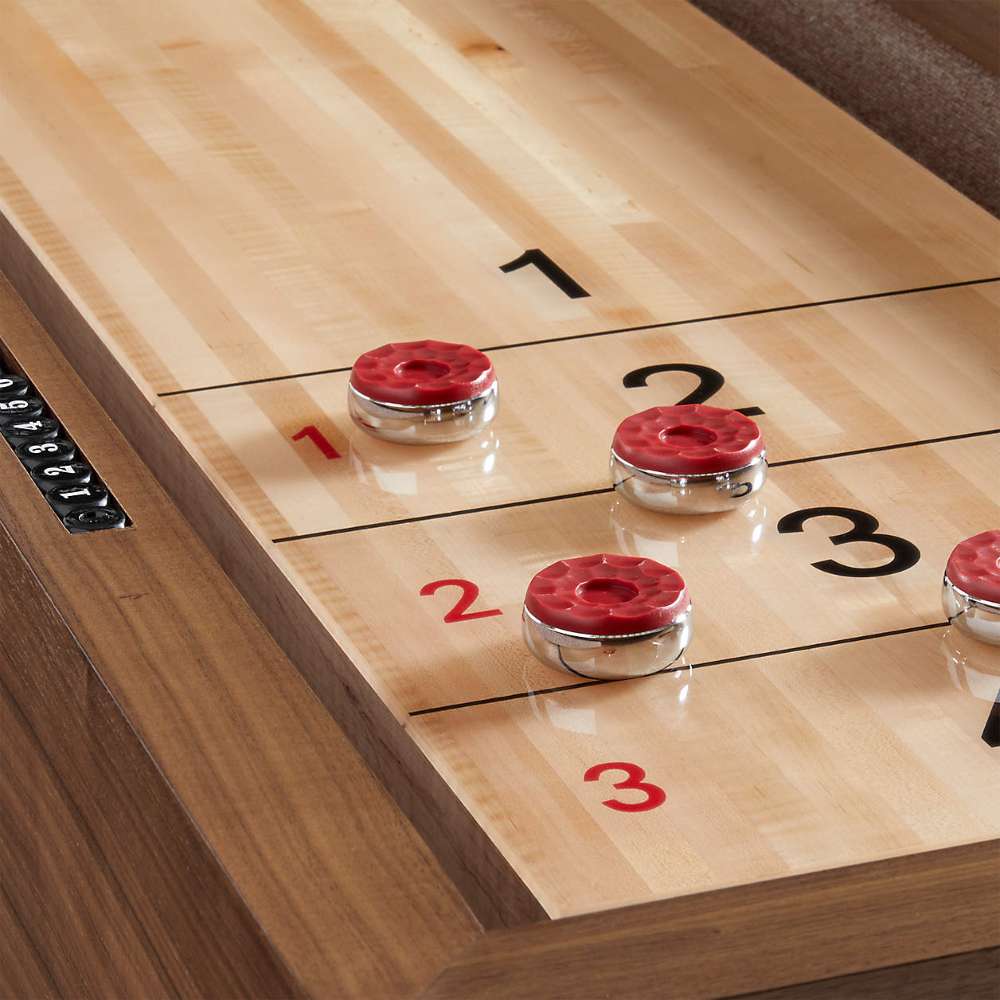 Walnut Crate & Barrel Shuffleboard in close up on the scoring zone with three red topped chrome pucks resting on the pale maple playfield beside the black and red numbers 1, 2 and 3
