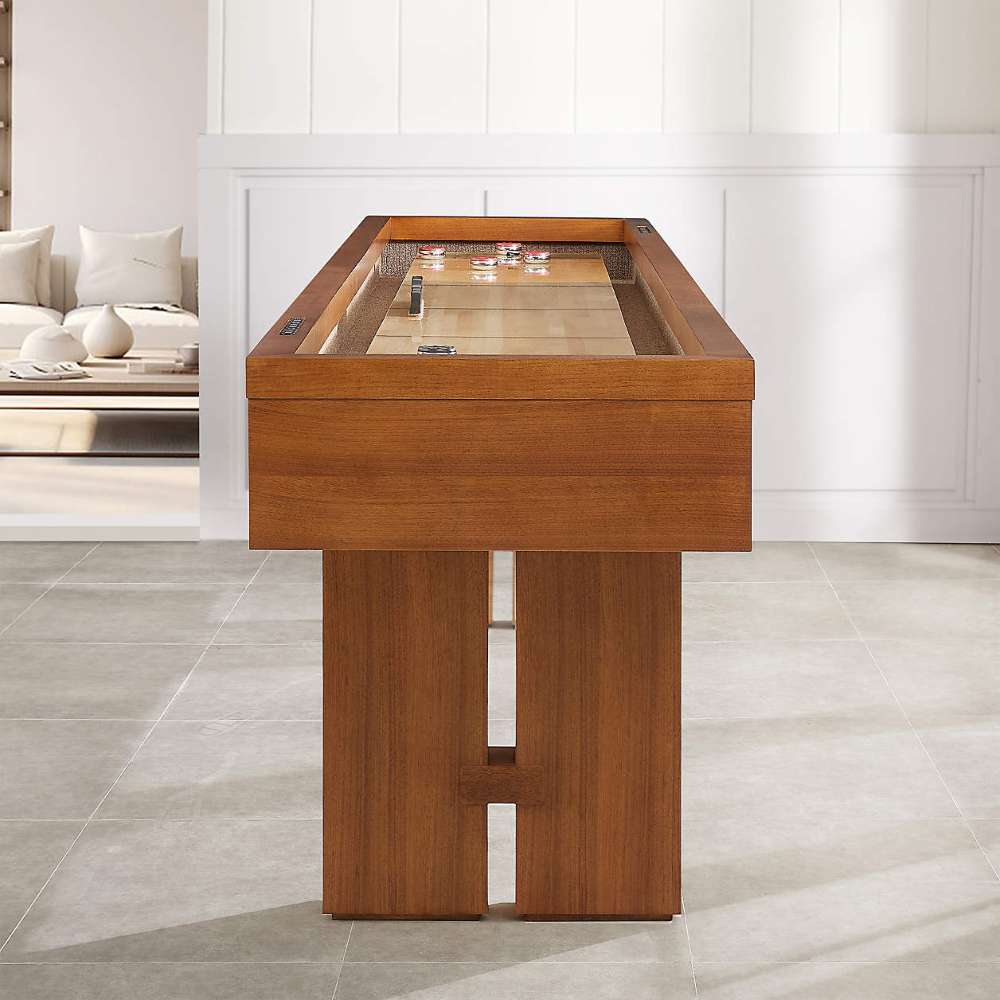 Walnut Crate & Barrel Shuffleboard seen end on in a room with white panelled walls and grey tile floors, looking down the pale maple playfield to pucks at the far end