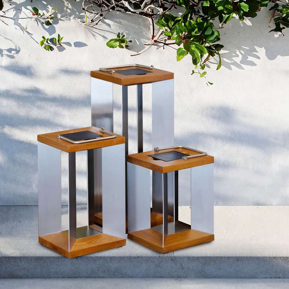 Weathered Teak Crate & Barrel Blade Teak and Stainless Steel LED Solar Outdoor Lantern shown in a styled outdoor setting, lit between its angled steel blades