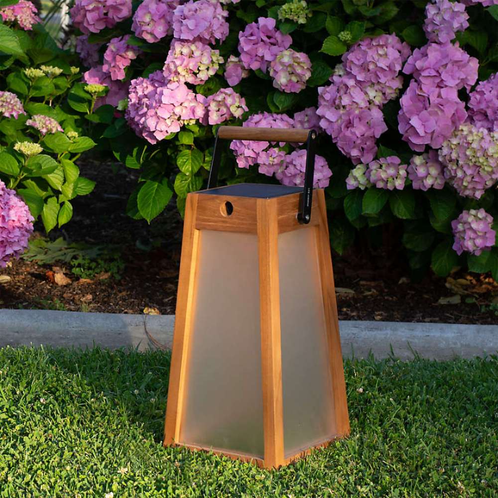 Weathered Teak Crate & Barrel Les Jardins Roam Teak LED Outdoor Solar-Powered Lantern 16" shown in a styled outdoor setting, cordless and carried by its aluminum and teak grip