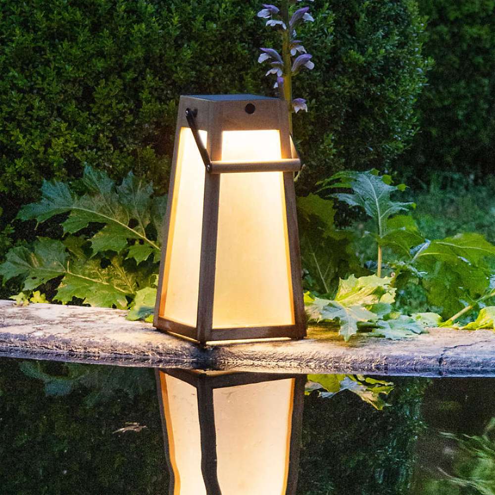 Weathered Teak Crate & Barrel Les Jardins Roam Teak LED Outdoor Solar-Powered Lantern 16" shown in a styled outdoor setting, its solar panel set into the top of the frame
