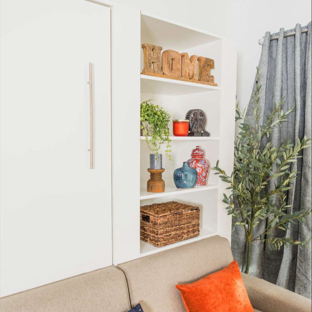 White Inovabed Wall Bed with Extended Sofa photographed corner view of the closed cabinet next to the bookcase styled with HOME letters, plants and woven baskets
