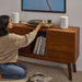 White Sonos Era 100 SL Compact Wireless Speaker a pair of the speakers flanking a record player on a walnut credenza as a woman kneels to pick a vinyl record from the shelf below