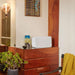 White Sonos Five Speaker sitting horizontally on top of a wooden chest of drawers beside a small vase with a yellow throw and a plant nearby