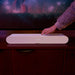 White Sonos Ray Sound Bar a hand reaching to the top of the bar on a dark wood cabinet below a television showing a concert, lit in pink