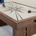 Woodgrain Crate & Barrel Air Hockey Table in close up at one corner showing the cream field with its grey starburst print, two black strikers, a sliding score counter in the rail and the black goal opening