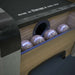 Woodgrain Crate & Barrel Skee-Ball Home Arcade Premium in close up on the ball return holding four speckled balls under blue light beside the words made in America since 1909